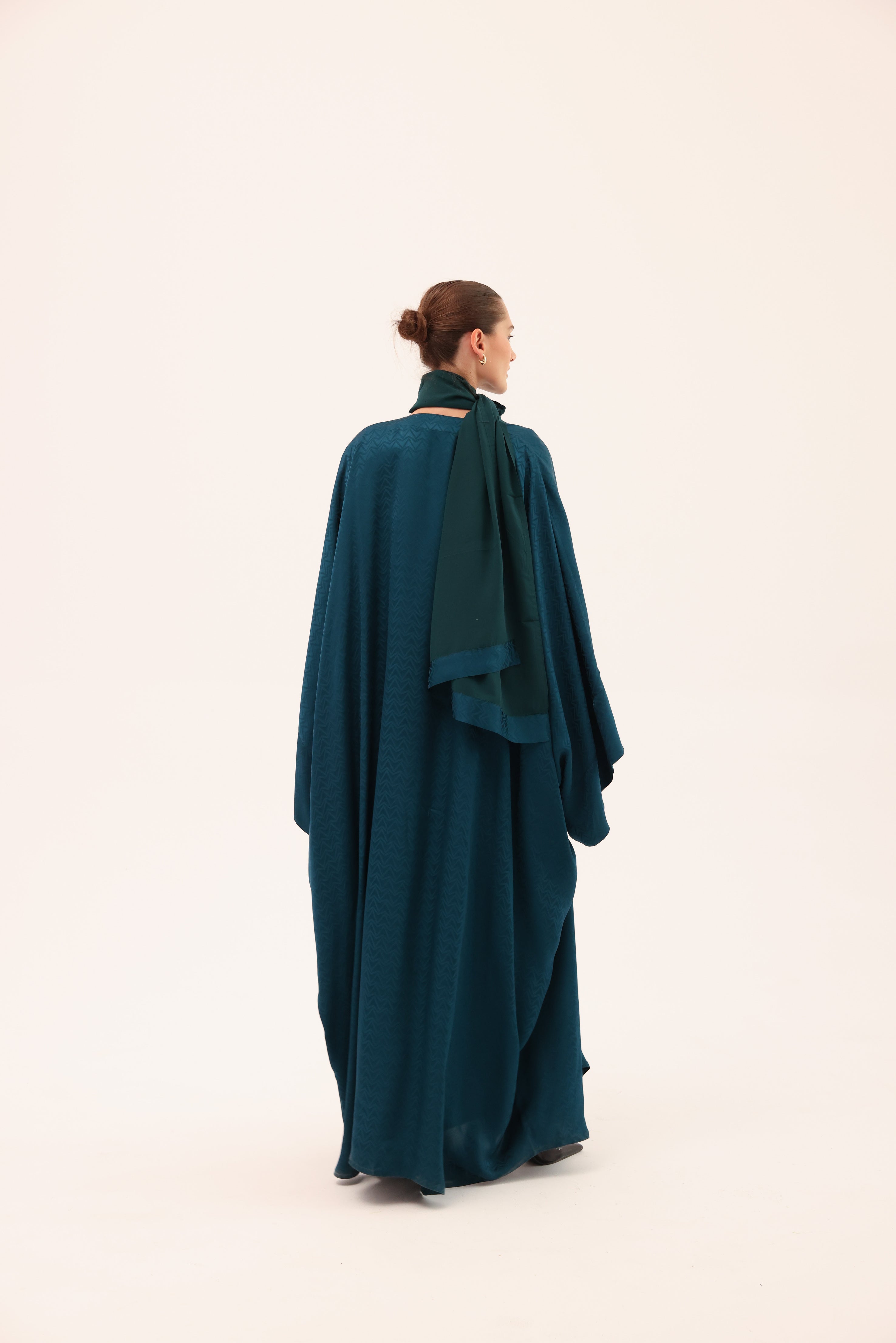 Model wearing the LUCE luxury turquoise silk abaya by Tre Sorelle, back view.