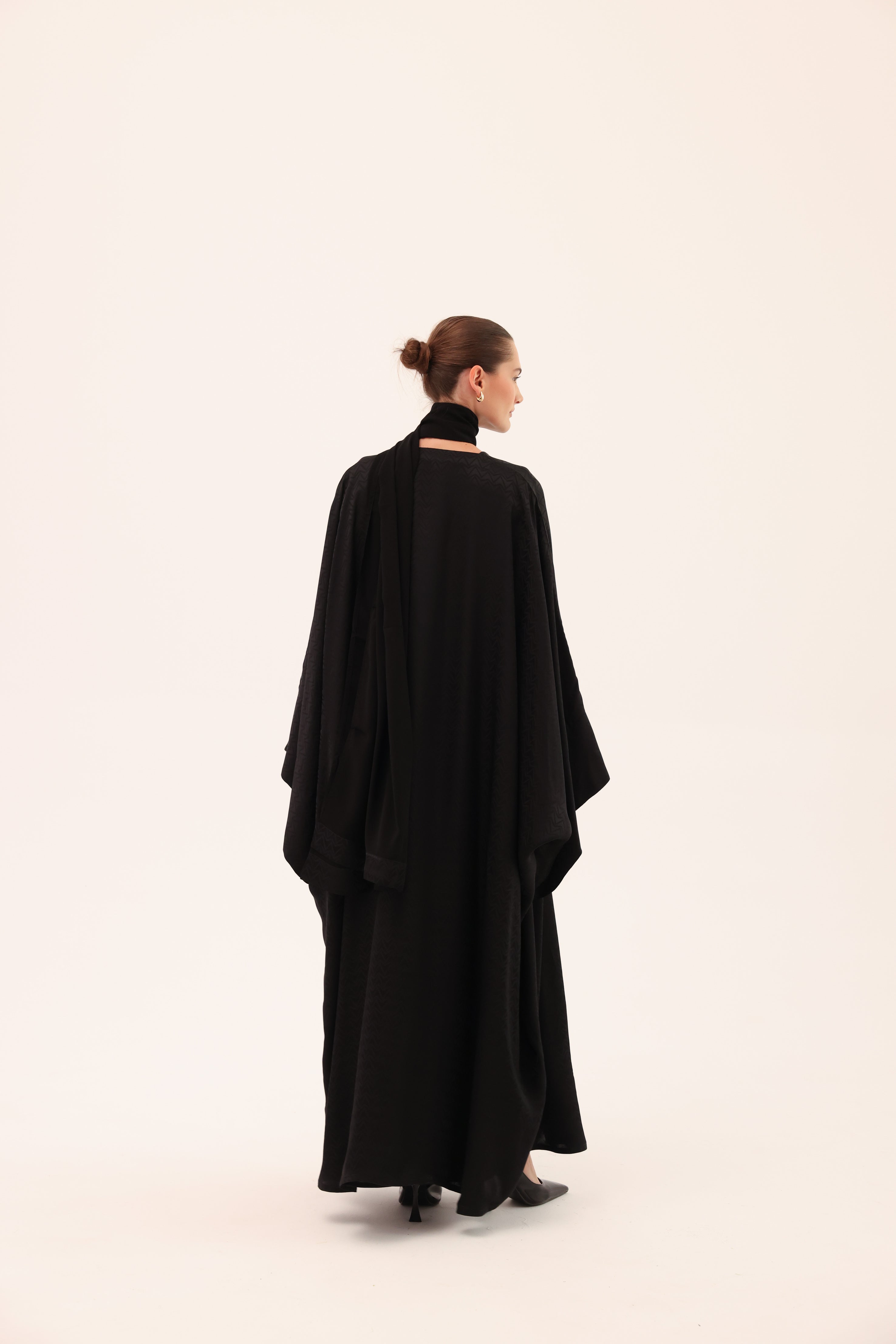 Model wearing the ARIA luxury black silk abaya by Tre Sorelle, back view.